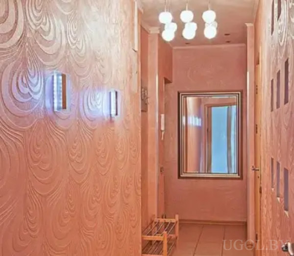 Коридор с текстурными розовыми стенами, подсветкой и большим зеркалом. На полу — плитка, у стены — обувница, а декоративные ниши добавляют глубины интерьеру.