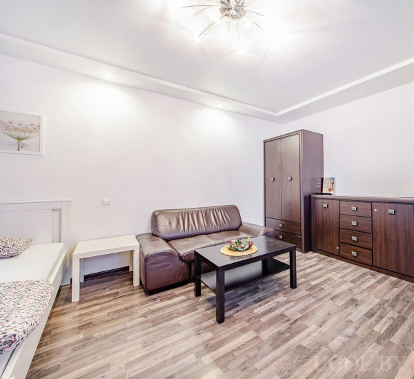 Интерьер с кожаным диваном, кроватью, столиком, шкафом, комодом и подвесным светильником.