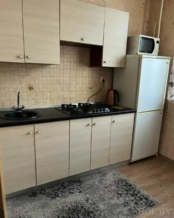 Кухня с черной столешницей, круглой мойкой, плитой на 4 конфорки, вытяжкой, белым холодильником и микроволновкой.