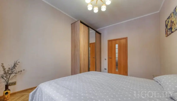 Комната с кроватью, зеркальным шкафом-купе, двумя дверями с матовым стеклом и декоративной вазой в углу.