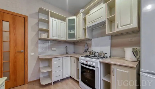 Компактная кухня с белыми шкафами, плитой на четыре конфорки, чайником и сушкой у угловой мойки.