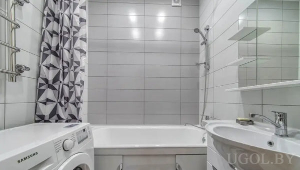 Современная ванная с белой ванной, душем, стиральной машиной «Samsung» и зеркалом с полками над раковиной.