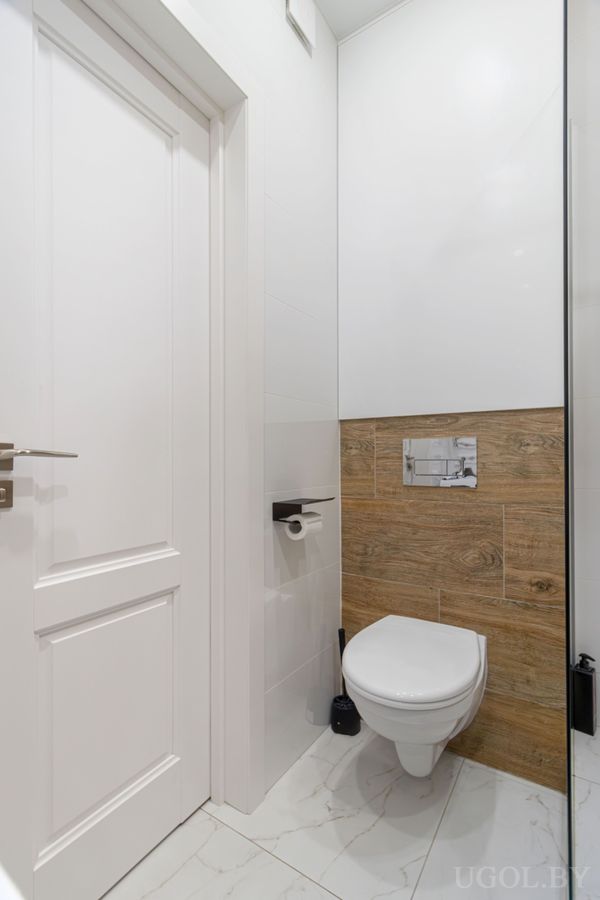 Минималистичная ванная с подвесным унитазом, деревянной плиткой на стене, белой дверью и мраморным полом.