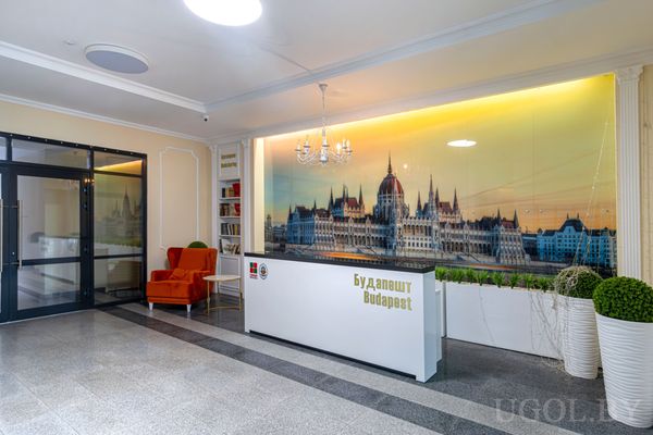 Интерьер зоны ресепшен с фото парламента, надписью Будапешт, оранжевым креслом, растениями и светлой отделкой.