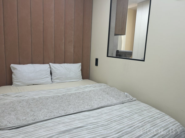 Современная спальня с белыми подушками, полосатым покрывалом и декоративным пледом, рядом окно или зеркало.