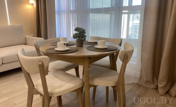 Круглый стол с четырьмя стульями, сервировка на каждого и центральное растение, рядом диван и панорамные окна.