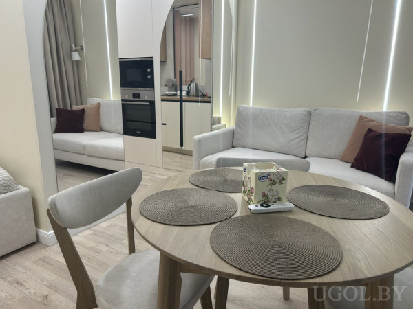 Обеденный стол на фоне кухни, два дивана с подушками, встроенные световые панели и арочный проход.