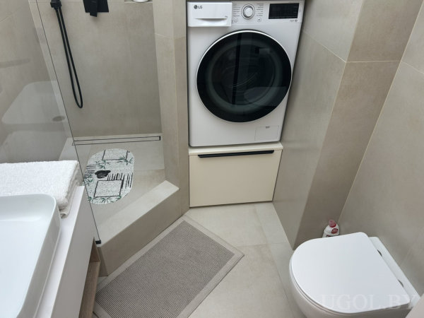 Компактная ванная с душем, белой раковиной, унитазом и стиральной машиной LG над встроенными ящиками.