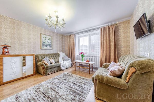 Светлая гостиная с двумя зелёными диванами, журнальным столиком с тюльпанами, телевизором и люстрой.