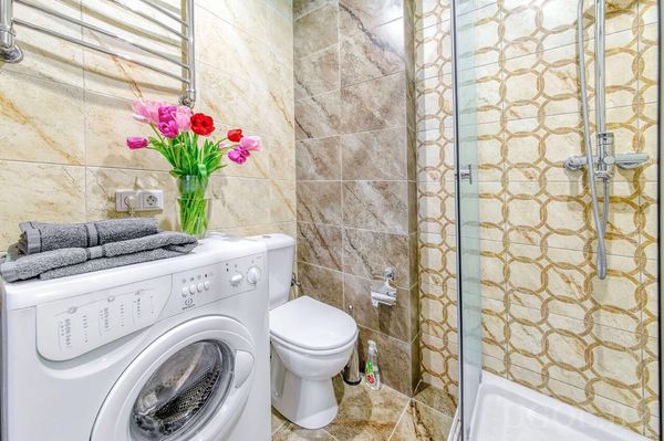 Современная ванная с белой стиральной машиной, красными полотенцами, туалетом и душевой кабиной.