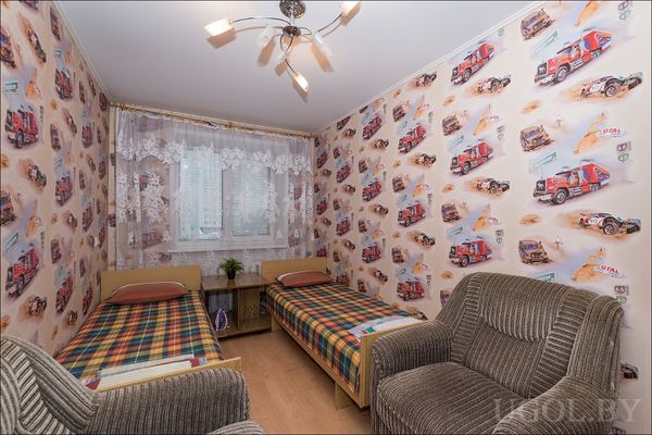 Детская с двумя односпальными кроватями, обоями с ралли и мягкими креслами. Светлая атмосфера и потолочный светильник.