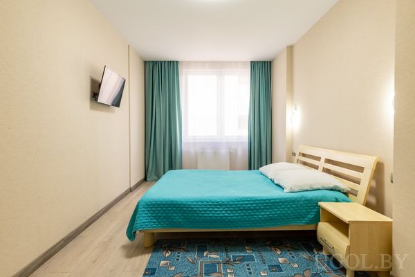 Спальня с двуспальной кроватью, бирюзовым текстилем и телевизором на стене