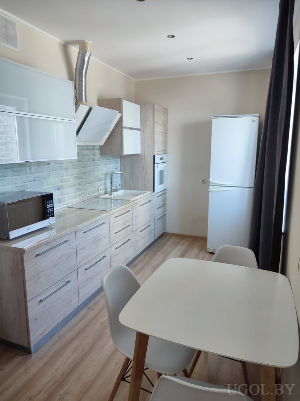 Современная кухня со светлыми деревянными фасадами, белым столом и стульями, плиточным фартуком и белой техникой.