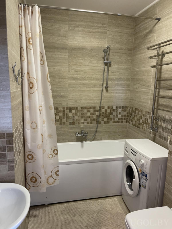 Бежевая ванная с ванной и душем, стиральной машиной, полотенцесушителем и занавеской с круговым узором.