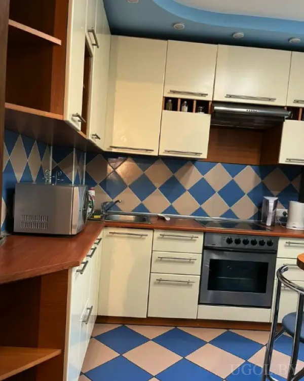 Кухонный гарнитур с кремовыми фасадами, плитка с синим и бежевым узором на полу и фартуке, встроенная техника и точечное освещение.