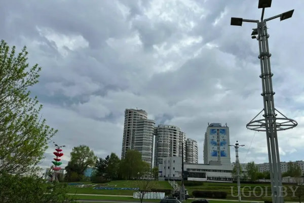 Вид на высотки, деревья и парковку, справа — фонарь, слева — яркая вертикальная скульптура, на фасаде одного здания — мурал или реклама.