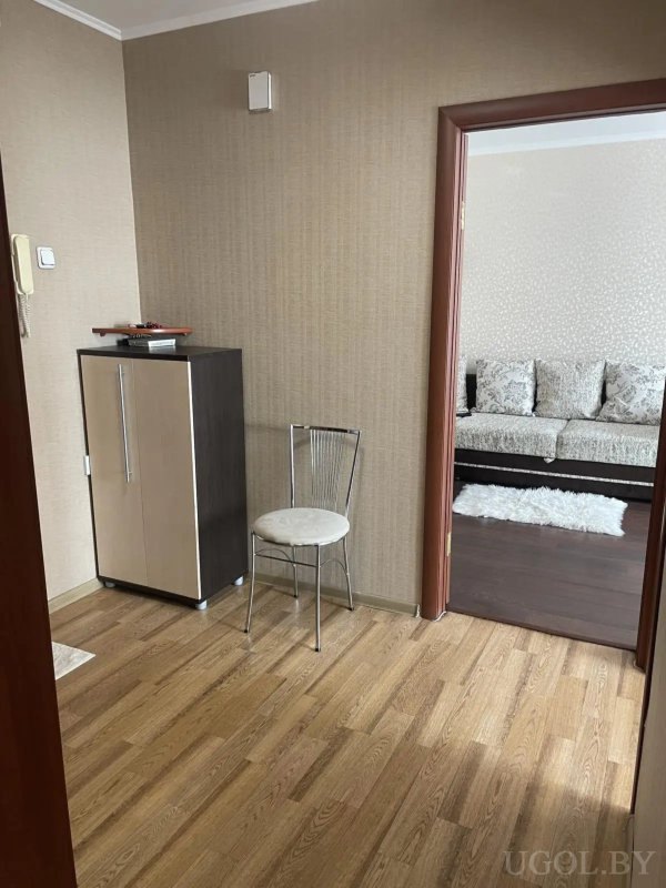 Вид на прихожую с тумбой и металлическим стулом, ведущую в гостиную с диваном и белым ковром.