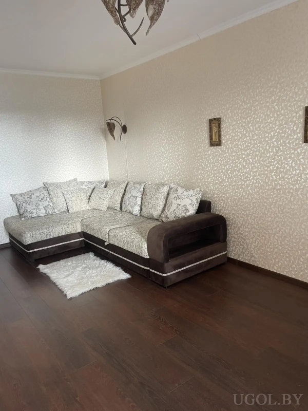 Светлая гостиная с угловым диваном, настенным светильником и декоративными элементами над диваном.