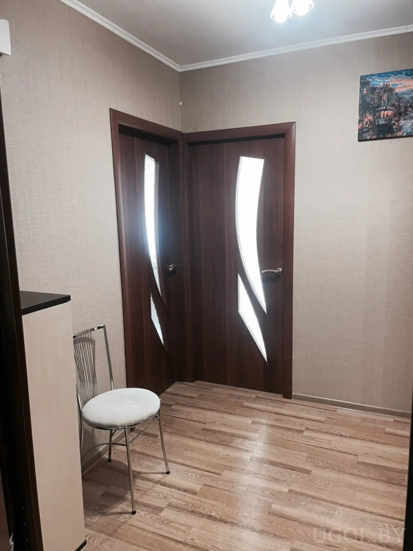 Входная зона с белым ковриком, тумбой, стулом и зеркальным шкафом с золотой рамкой.