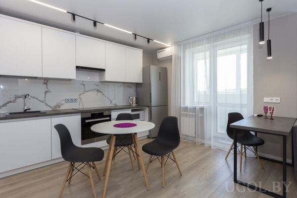 Кухонная зона с белыми шкафами, мраморным фартуком, круглым столом и барной стойкой с двумя бокалами.