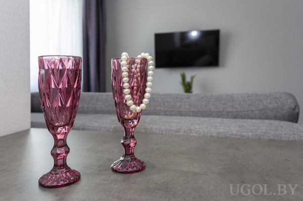 Композиция с двумя бокалами, ниткой жемчуга, серым диваном и телевизором на фоне.