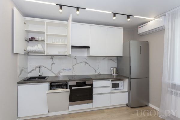 Интерьер с белыми шкафами, открытой машиной, техникой, мраморным фартуком и кондиционером над холодильником.