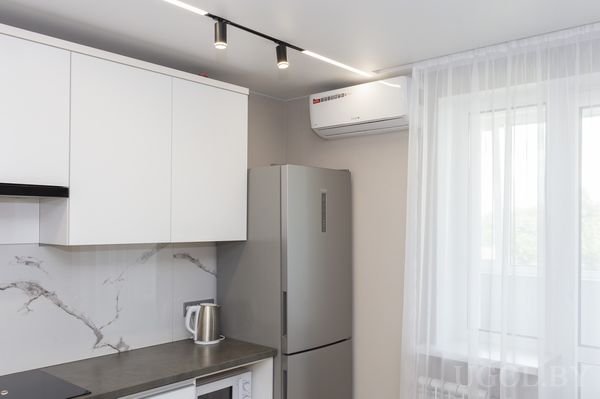 Кухонная зона с белыми шкафами, серым фартуком, холодильником, чайником и точечным освещением.