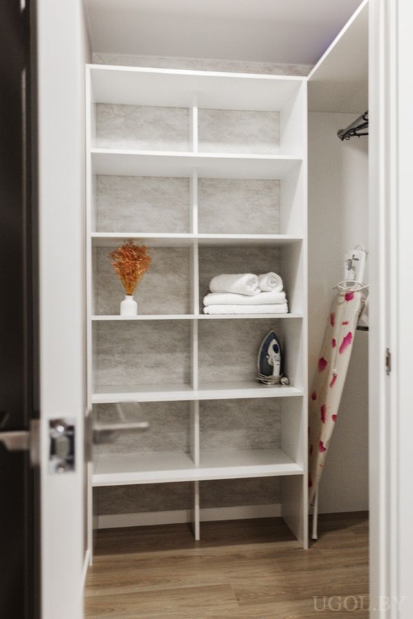 Ниша с белыми полками, утюгом, вазой с сухоцветами, стопкой полотенец и доской с сердечками.