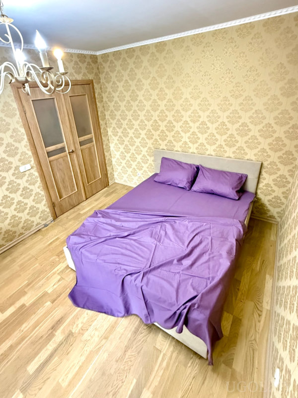 Классический интерьер с двуспальной кроватью, сиреневыми простынями и обоями с дамасским узором.