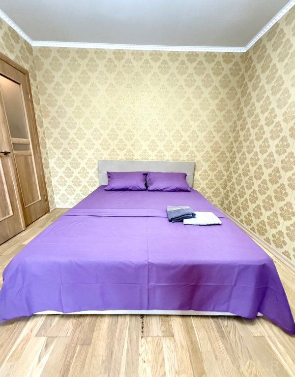 Элегантная комната с сиреневым постельным бельём и аккуратно сложенными полотенцами на фоне золотого орнамента.