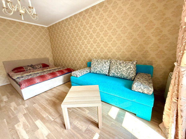 Уютное пространство с кроватью, ярким бирюзовым диваном и кофейным столиком на фоне светлых обоев.