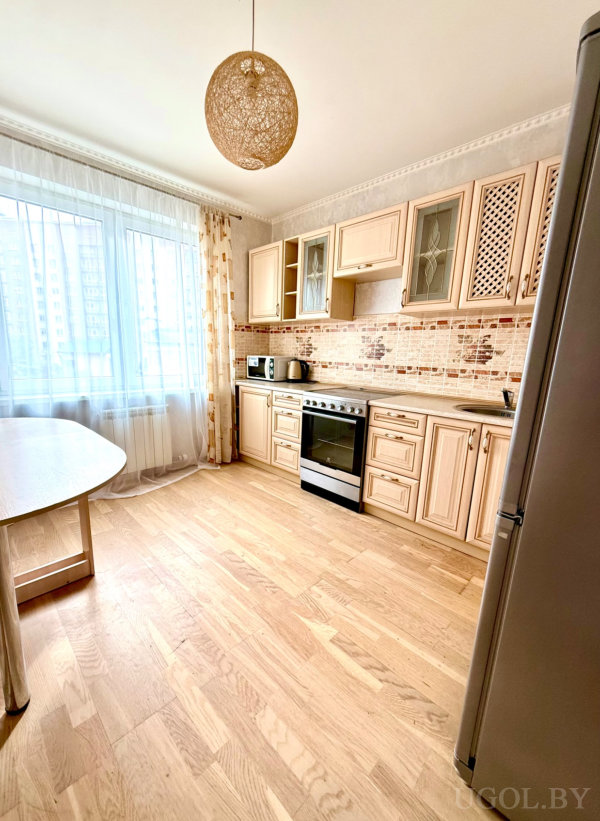 Светлая кухня с декоративными шкафами, плиткой в бежевых тонах и техникой на фоне большого окна.