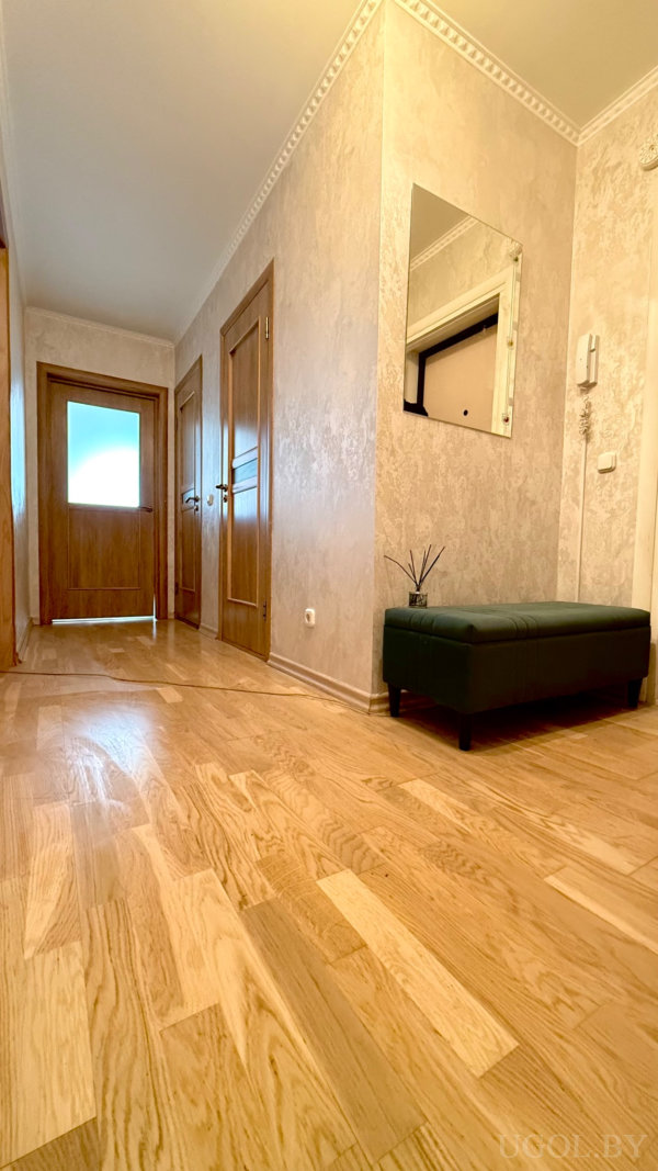 Светлый коридор с деревянными дверями, банкеткой, зеркалом и элементами декора в нейтральных тонах.