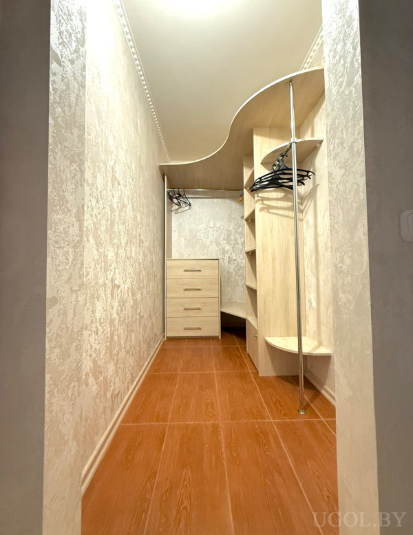 Узкое пространство с вешалкой, комодом и угловыми полками, оформленное в светлых древесных оттенках.