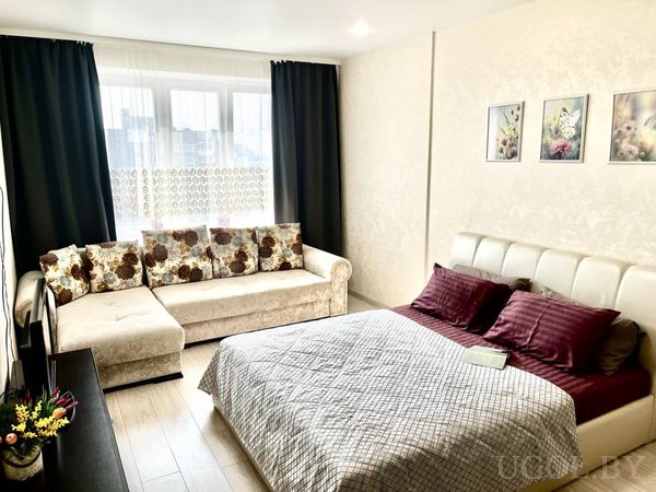 Современная спальня с белым изголовьем, серым покрывалом, бордовыми подушками и кремовым диваном с цветочными подушками.