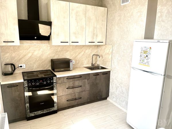 Кухня с плитой, вытяжкой, микроволновкой, чайником и белым холодильником с магнитами.