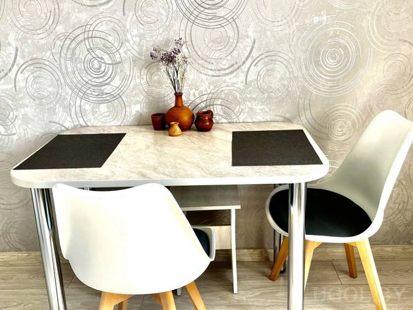 Небольшая обеденная зона с белым столом, двумя стульями и декоративными вазами на фоне серой стены.