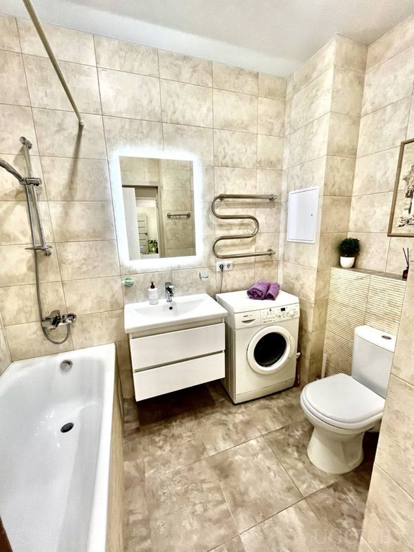 Современная ванная с ванной, раковиной, стиральной машиной, унитазом и полотенцесушителем.