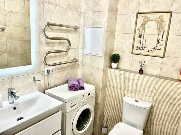 Компактная ванная с раковиной, стиральной машиной, унитазом, полотенцесушителем и декором над полкой.