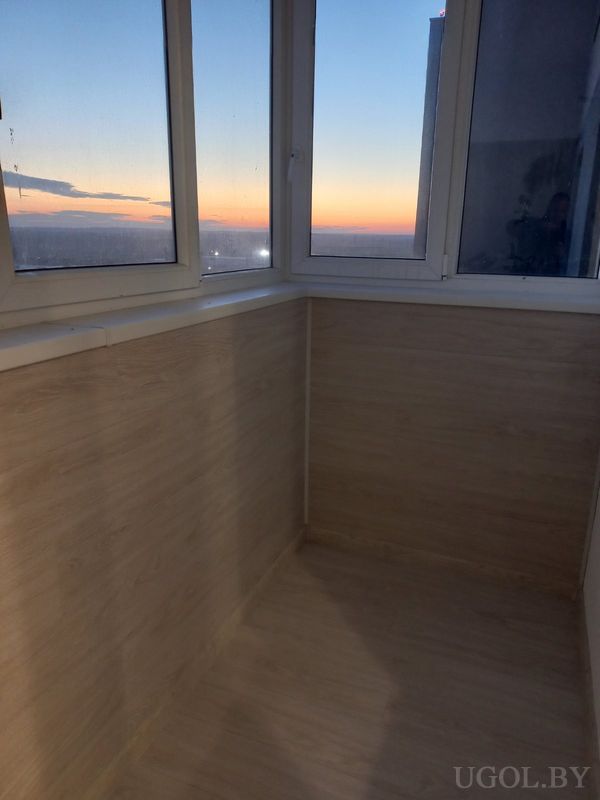 Застеклённый балкон с деревянной отделкой и видом на закат над городом.