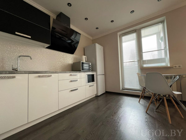 Белые нижние и чёрные верхние фасады, вытяжка, холодильник, стеклянный круглый стол и белые стулья у окна.