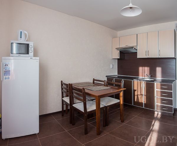 Минималистичная кухня с белым холодильником, деревянным столом на четыре персоны и варочной панелью.