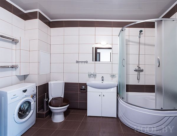 Функциональная ванная с душевой кабиной, стиральной машиной, белой раковиной и комбинированной плиткой.