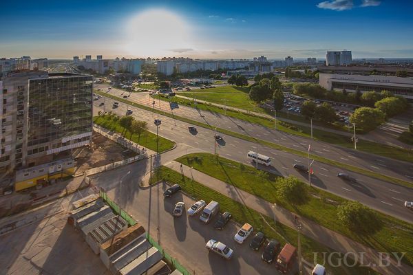 Панорамный вид из окна на городской пейзаж и парковку перед домом, с элементами освещения.