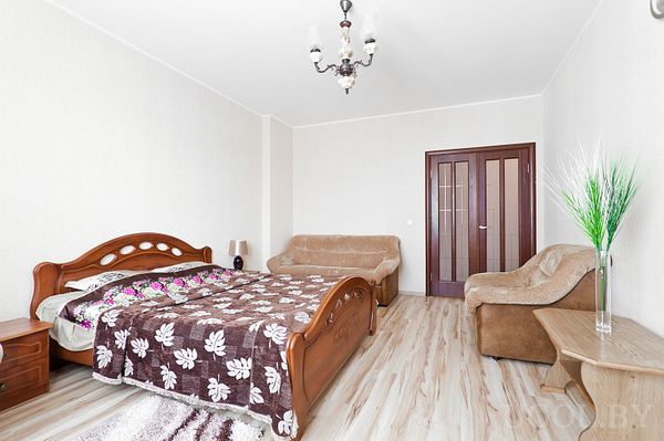 Комната с двуспальной кроватью, диваном, креслом и декоративной вазой. Деревянные двери, люстра, чистый ламинат и спокойная атмосфера.