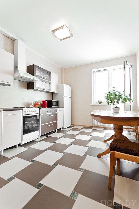 Функциональная кухня с плиткой в шахматном стиле, техникой, обеденным столом и большим окном. Есть холодильник, микроволновка и чайник.