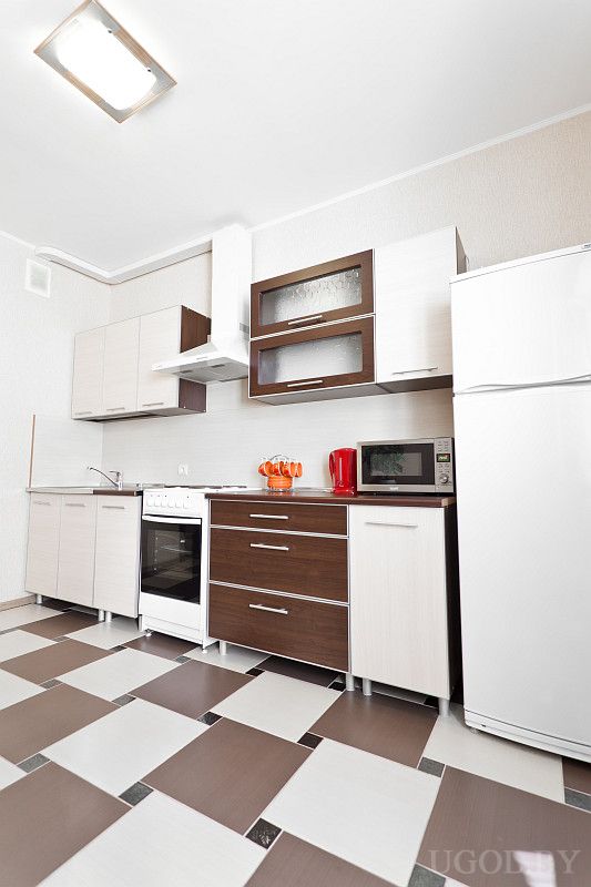 Современная кухня с белой плитой, вытяжкой, красным чайником и комплектом оранжевых чашек. Чистая рабочая зона и удобная планировка.