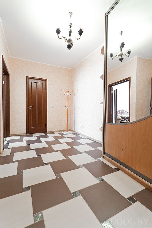 Просторный коридор с плиткой, зеркальным шкафом и черной люстрой. Есть вешалка и деревянные двери.