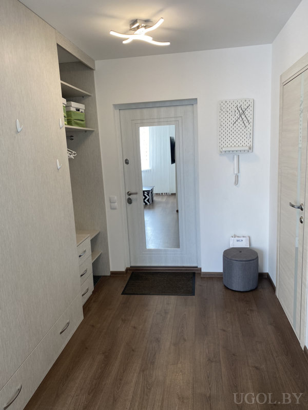 Зона входа с тумбой, зеркалом, светильником, пуфом, ящиками и белыми стенами.