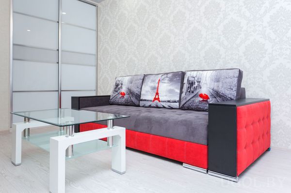 Интерьер с диваном, подушками с принтами, стеклянным столом, узорчатой стеной и дверью с матовыми вставками.